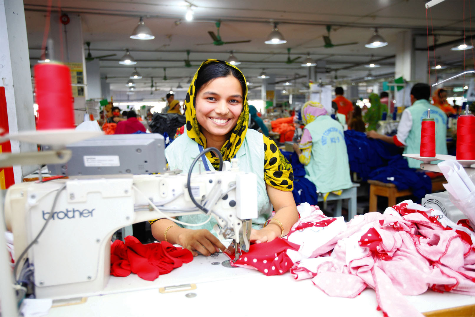 A woman garments worker is smiling while sewing. 